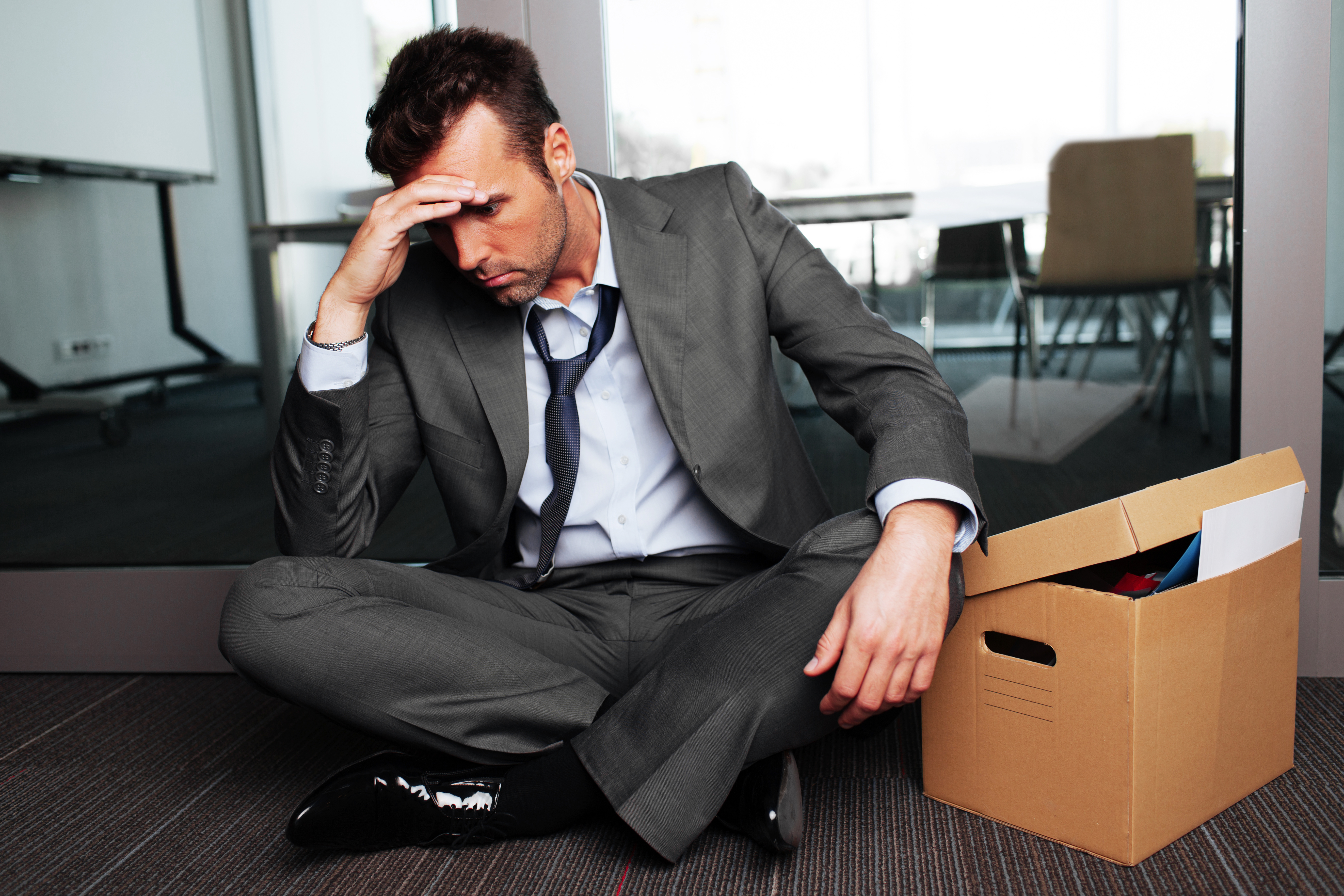 Sad fired businessman sitting outside meeting room after being dismissed