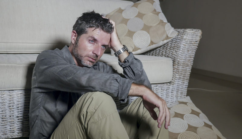 lifestyle portrait young attractive sad and depressed man sitting on living room floor feeling desperate and stressed suffering depression and anxiety problem looking frustrated and worried