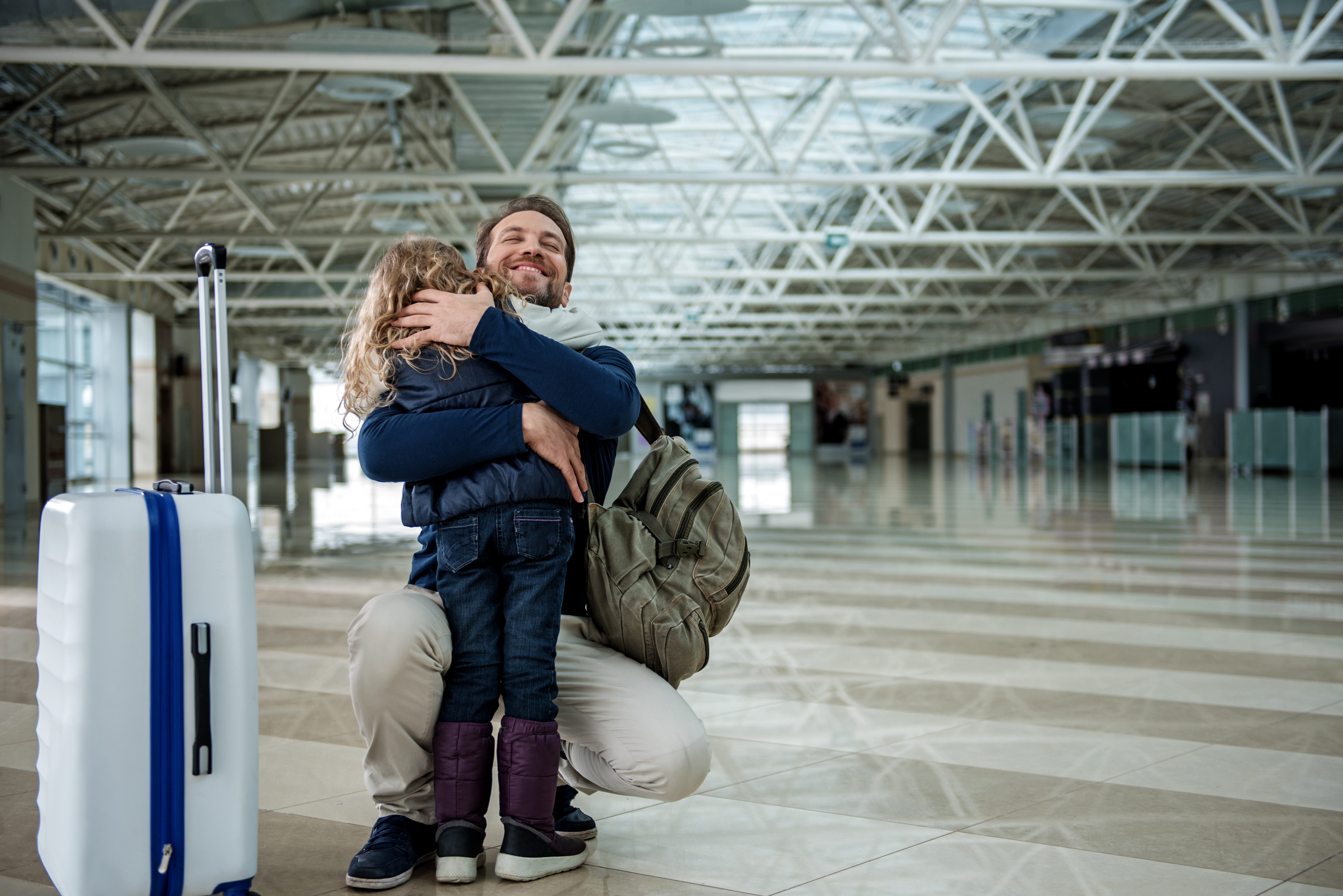 Daddy is embracing girl in the airport hall with happiness. Copy space in right side