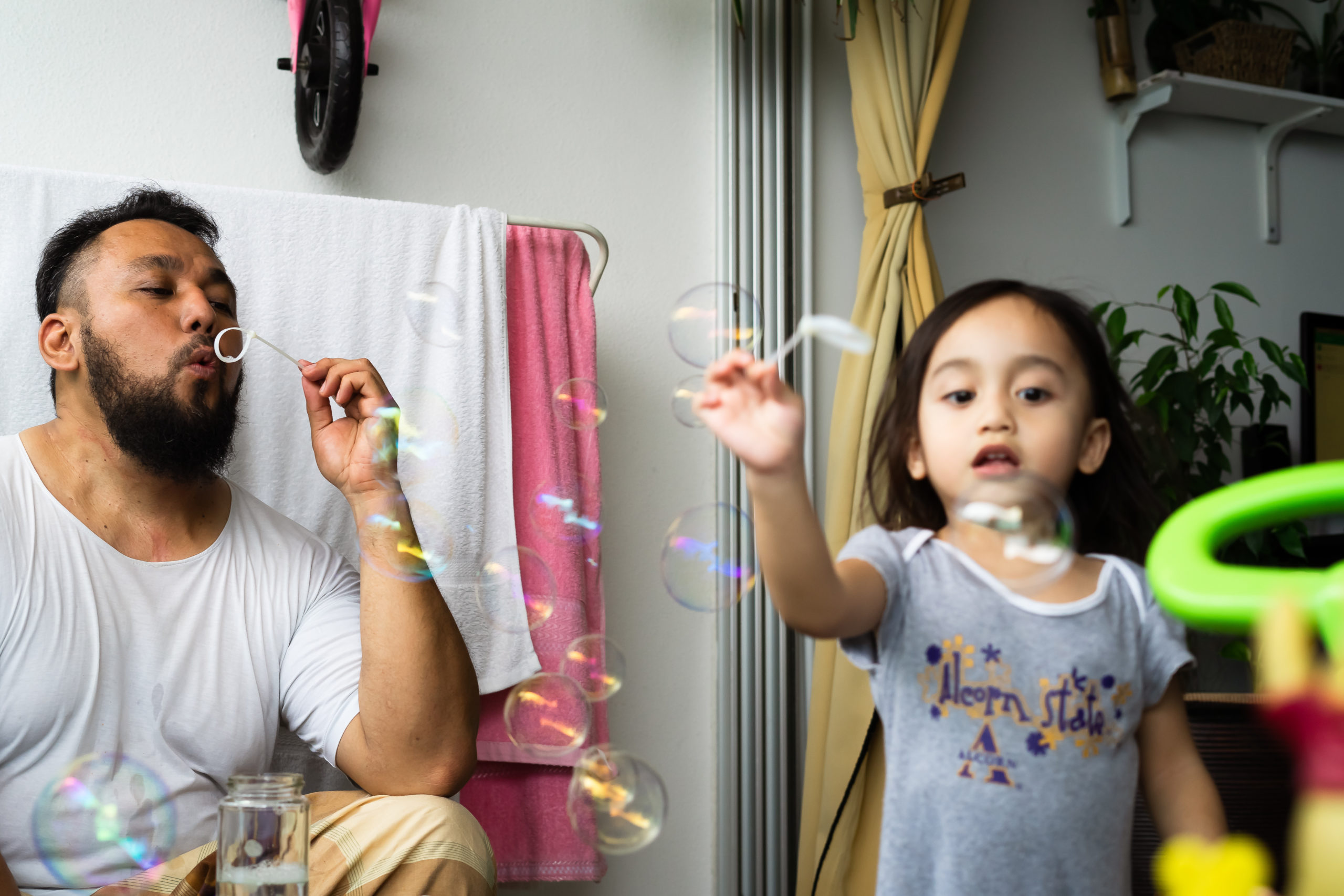 Bangi, Malaysia - April 16, 2020: Father playing soap bubbles with child at home. Stay home during lockdown due to Coronavirus, Covid 19 outbreak. Selective focus.